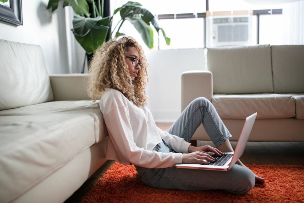 Imagem de uma mulher sentada no chão da sala com um notebook em suas pernas