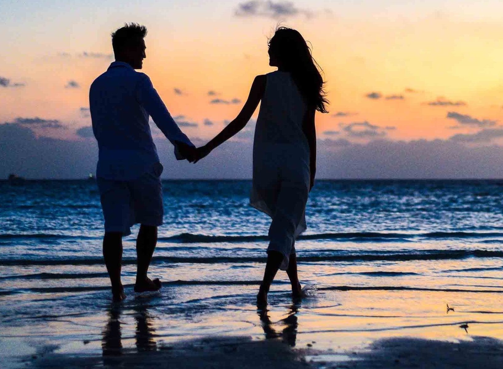 man and woman holding hands walking on seashore during 1024960 e1573582404165