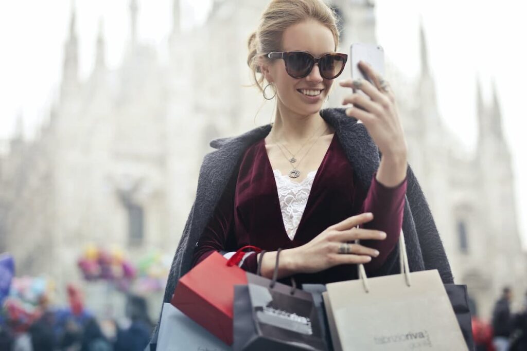 Imagem de uma mulher conversando no celular segurando sacolas de compras
