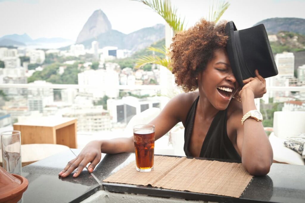 Imagem de uma mulher rindo com um chapéu tomando um drink
