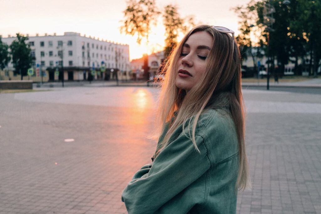 Imagem de uma mulher loira em uma praça sozinha de olhos fechados