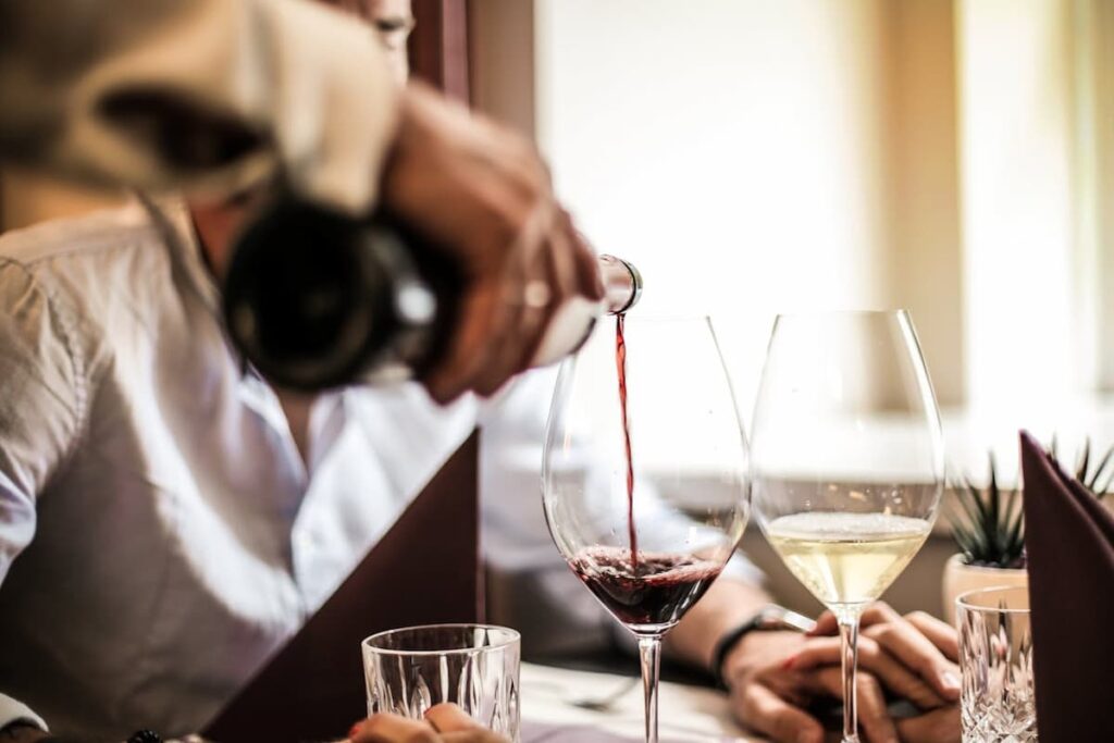 Imagem de uma mesa com taças com o garçom servindo vinho